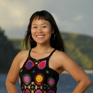 Mary Zheng, hands on hips, smiling broadly, wearing a colorful crocheted dress. 